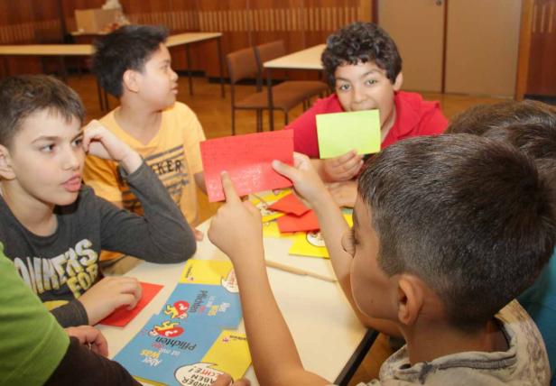 Eine Gruppe von Kindern sitzt an einem Tisch und spielt mit farbigen Karten.
