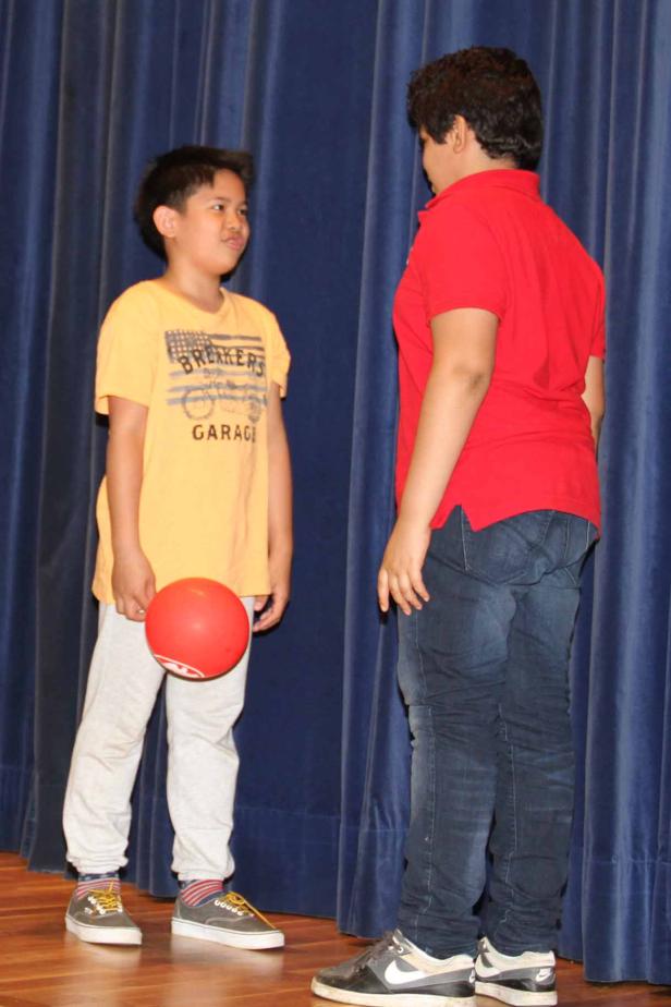 Zwei Jungen stehen vor einem blauen Vorhang, einer hält einen roten Ballon.