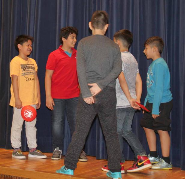 Fünf Jungen stehen auf einer Bühne vor einem blauen Vorhang.