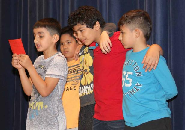Eine Gruppe von vier Jungen steht zusammen, einer liest von einem roten Zettel ab.
