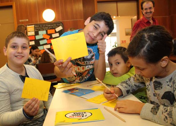Eine Gruppe Kinder sitzt an einem Tisch und malt auf gelbem Papier.