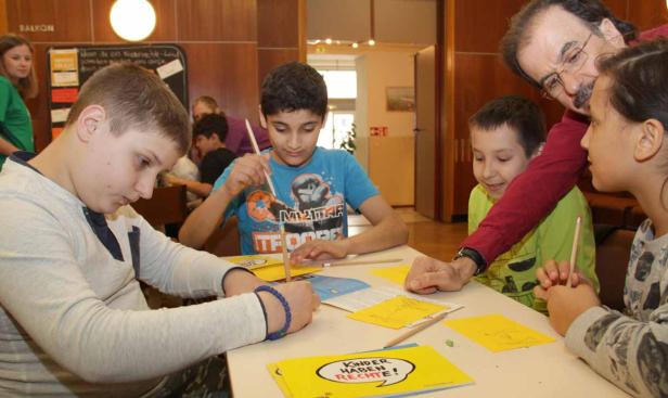 Eine Gruppe von Kindern sitzt mit einem Lehrer an einem Tisch und malt Bilder zum Thema Kinderrechte.