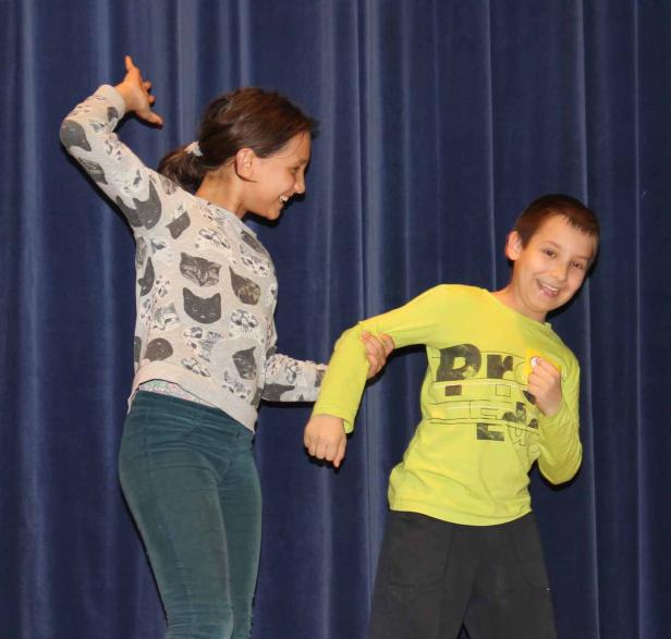 Ein Mädchen hält den Arm eines Jungen vor einem blauen Vorhang fest.