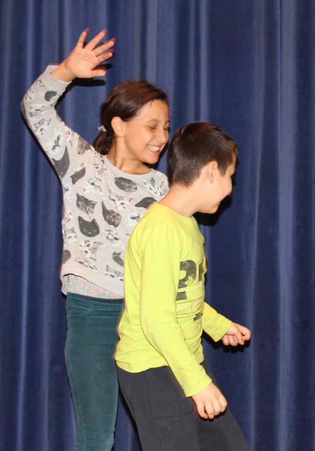 Ein Mädchen und ein Junge stehen lachend vor einem blauen Vorhang.