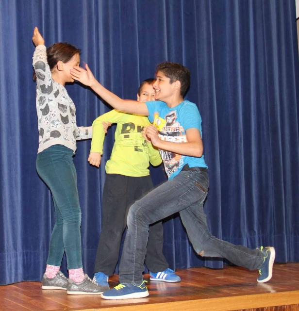 Drei Kinder spielen auf einer Bühne vor einem blauen Vorhang.