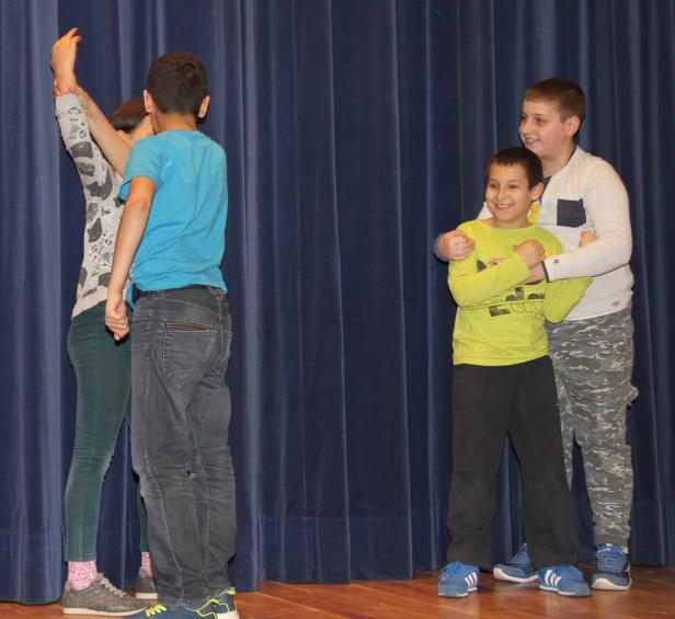Vier Kinder stehen auf einer Bühne vor einem blauen Vorhang.