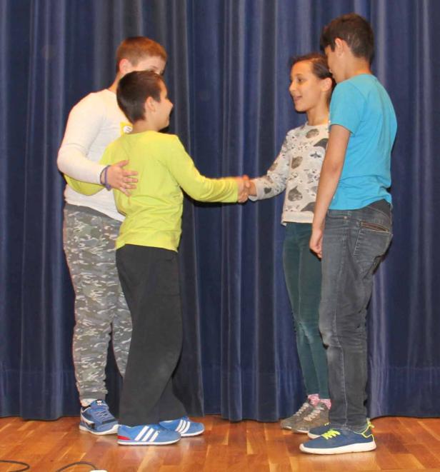 Vier Kinder stehen auf einer Bühne und schütteln sich die Hände.