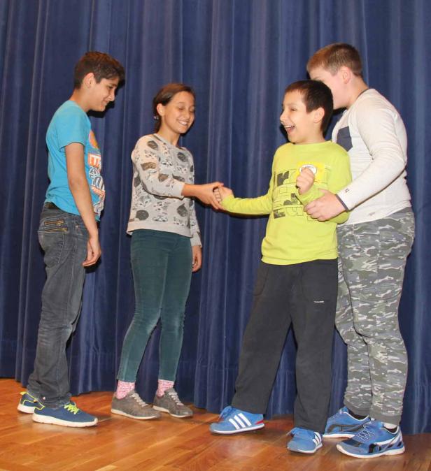 Vier Kinder stehen auf einer Bühne, ein Junge gratuliert einem anderen per Handschlag.