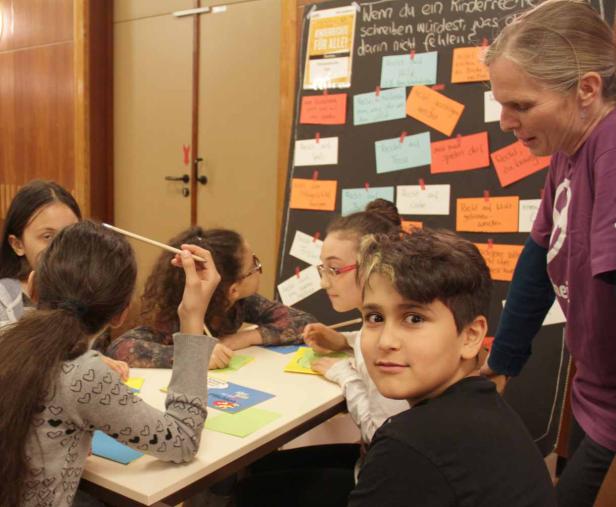 Eine Gruppe Kinder sitzt mit einer Lehrerin an einem Tisch und diskutiert über Kinderrechte.