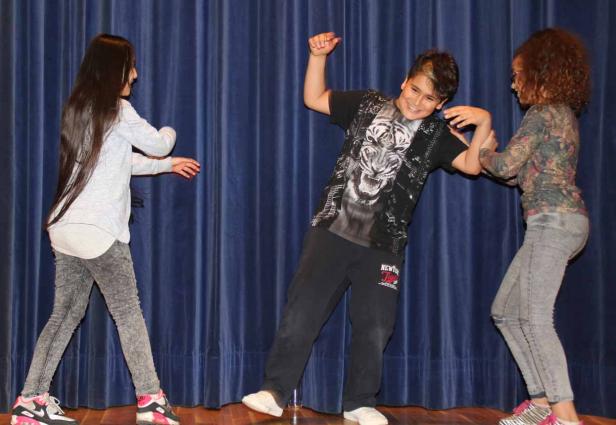 Drei Kinder tanzen auf einer Bühne vor einem blauen Vorhang.
