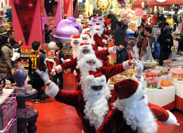Eine Gruppe von als Weihnachtsmänner verkleideten Menschen tanzt in einem Süßwarenladen.