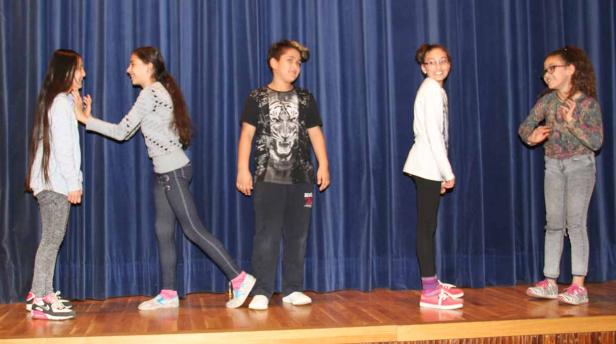 Fünf Kinder stehen auf einer Bühne vor einem blauen Vorhang.