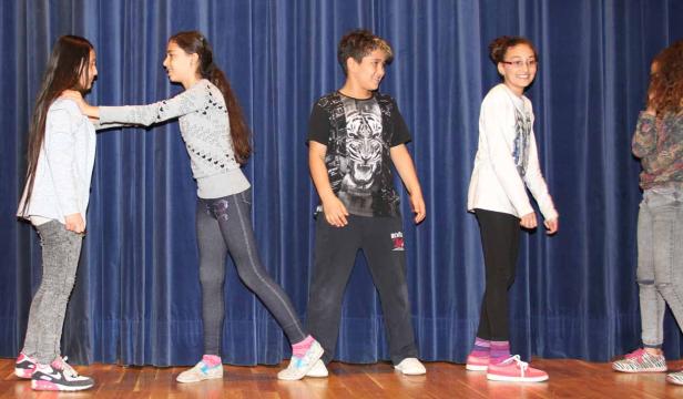Eine Gruppe von Teenagern steht auf einer Bühne vor einem blauen Vorhang.