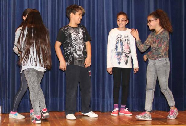 Eine Gruppe von vier Kindern steht auf einer Bühne vor einem blauen Vorhang.