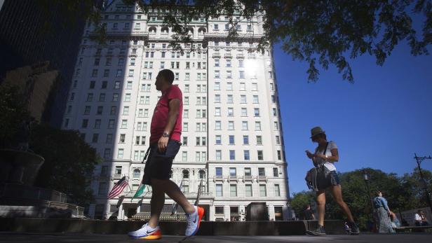 Zwei Personen gehen an einem sonnigen Tag vor dem Plaza Hotel in New York entlang.