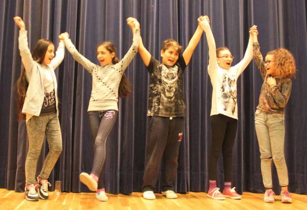 Fünf Kinder stehen auf einer Bühne vor einem Vorhang und halten Händchen.