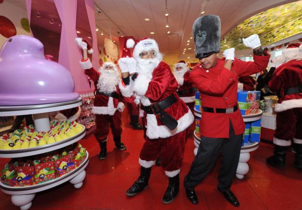 Mehrere als Weihnachtsmänner verkleidete Personen und ein Mann in roter Uniform posieren in einem Süßwarenladen.