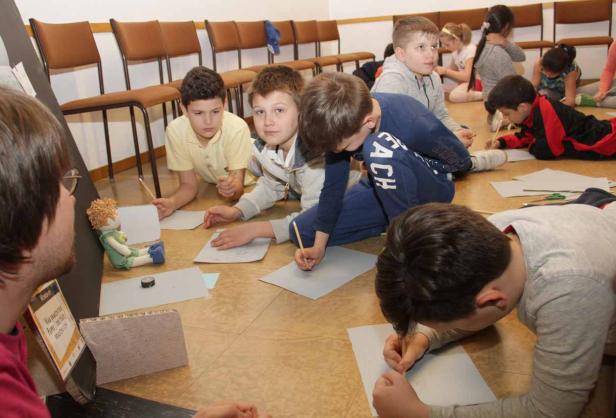 Eine Gruppe Kinder liegt auf dem Boden und zeichnet auf Papier.