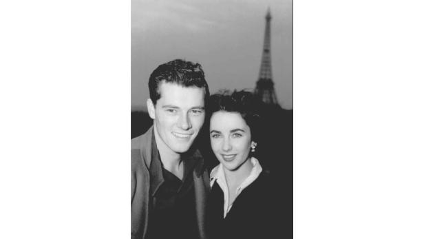 Ein Schwarzweißfoto von Elizabeth Taylor und ihrem damaligen Ehemann Michael Wilding vor dem Eiffelturm.