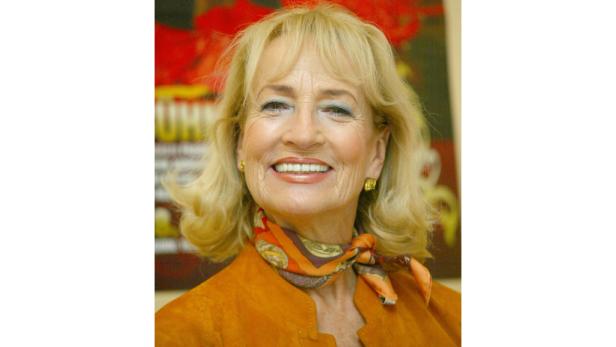 Eine lächelnde Frau mit blonden Haaren und einem orangefarbenen Schal um den Hals.