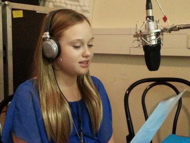 Eine junge Frau mit Kopfhörern liest einen Text vor einem Mikrofon.