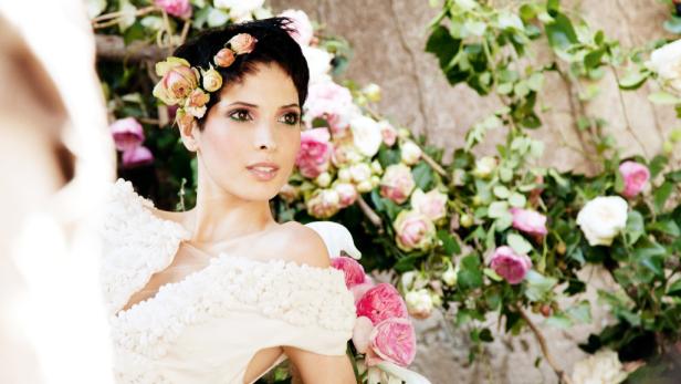 Eine Frau mit Blumen im Haar posiert vor einem Hintergrund aus Rosen.