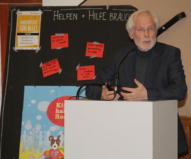 Ein älterer Mann spricht an einem Rednerpult vor einer Tafel zum Thema Kinderrechte.