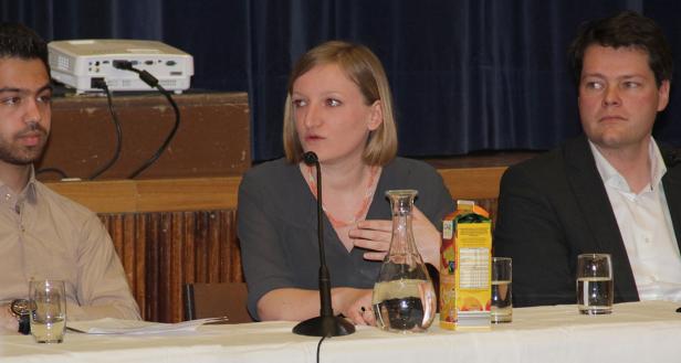 Drei Personen sitzen an einem Tisch während einer Podiumsdiskussion.