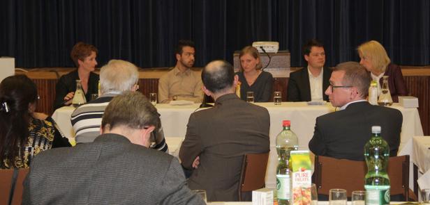 Mehrere Personen sitzen an einer langen Tafel bei einer Konferenz oder einer Podiumsdiskussion.