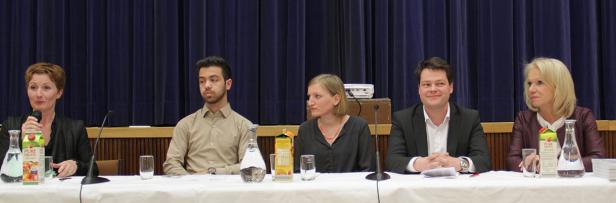 Fünf Personen sitzen an einem Tisch vor einem blauen Vorhang während einer Podiumsdiskussion.
