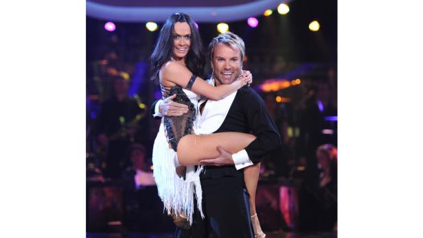 Ein Mann trägt eine Frau in einem weißen Kleid auf einer Bühne.