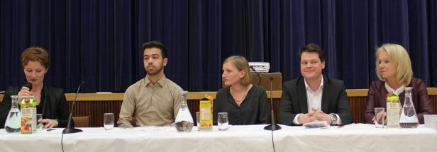 Fünf Personen sitzen an einem Tisch vor einem blauen Vorhang.