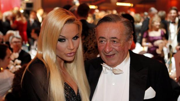 Eine blonde Frau und ein älterer Mann im Smoking posieren auf einer Gala.