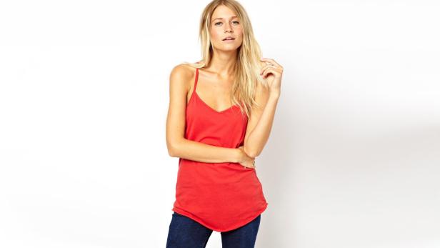 Eine Frau mit blonden Haaren trägt ein rotes Tanktop und Jeans.