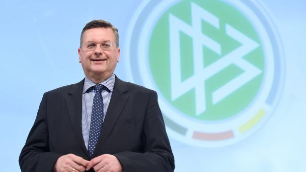Ein Mann mit Brille und Anzug steht vor dem Logo des DFB.