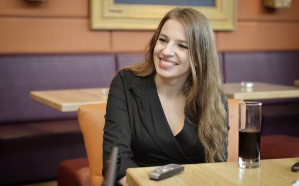 Eine lächelnde Frau sitzt in einem Restaurant an einem Tisch mit einem Getränk.