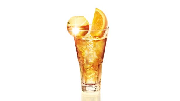 Ein Glas Metaxa mit Eis, einer Orangenscheibe und einer Cocktailkugel.