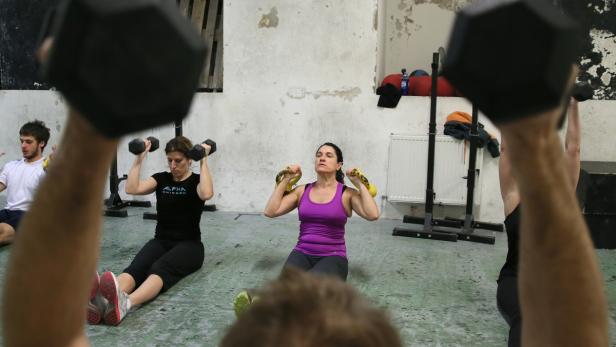 Eine Gruppe von Menschen trainiert mit Hanteln und Kettlebells in einem Fitnessstudio.