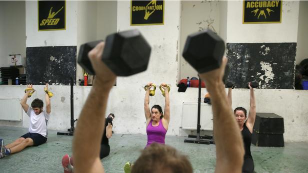 Eine Gruppe von Menschen trainiert in einem Fitnessstudio mit Gewichten und Kettlebells.