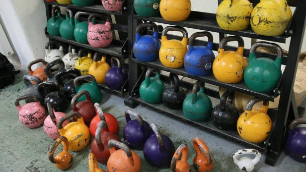 Mehrfarbige Kettlebells stehen in einem Regal und auf dem Boden.