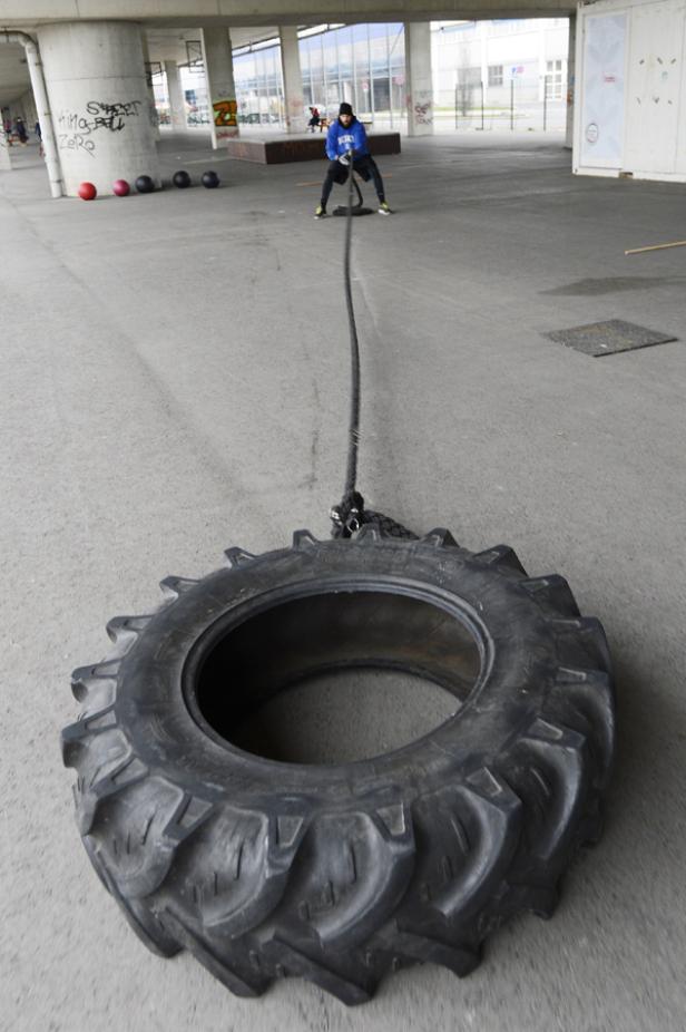 Ein Mann zieht einen Traktorreifen mit einem Seil unter einer Brücke.