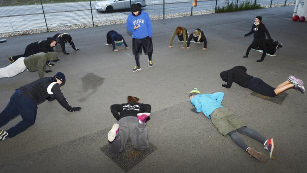 Eine Gruppe von Menschen trainiert unter freiem Himmel, angeleitet von einem Trainer.