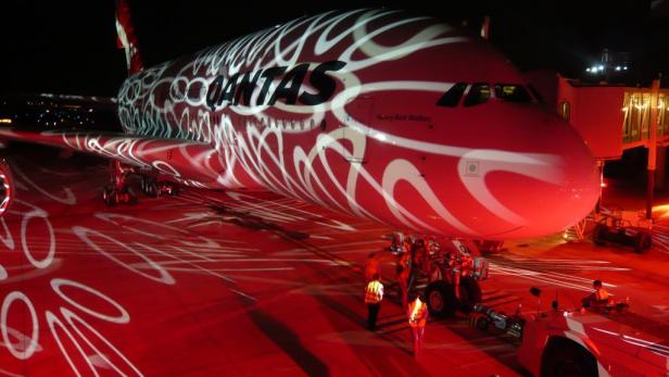 Ein Qantas-Flugzeug mit spezieller Lackierung steht nachts auf dem Rollfeld.
