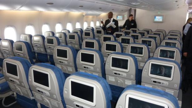 Blick in das Innere eines Flugzeugs mit blauen Sitzen und Bildschirmen.