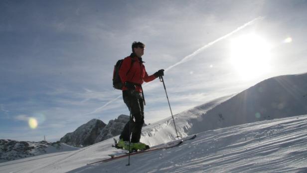 Ein Skifahrer mit Rucksack steigt einen schneebedeckten Hang hinauf.