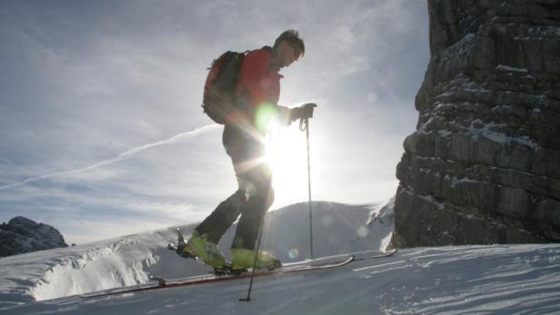 Ein Skifahrer steigt mit Skiern und Stöcken einen schneebedeckten Hang hinauf.