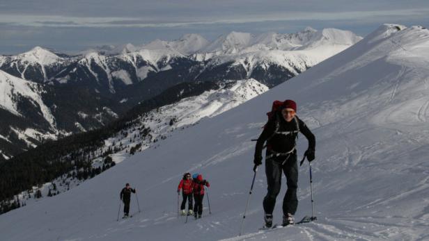 Eine Gruppe von Skitourengehern steigt einen schneebedeckten Hang hinauf.