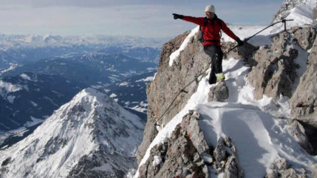 Ein Bergsteiger auf einem schneebedeckten Gipfel mit Blick auf eine Bergkette.