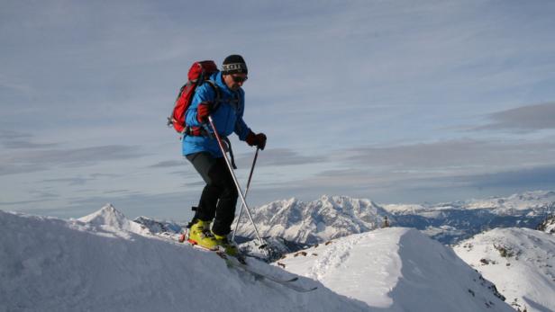 Ein Skifahrer mit rotem Rucksack fährt einen schneebedeckten Hang hinunter.