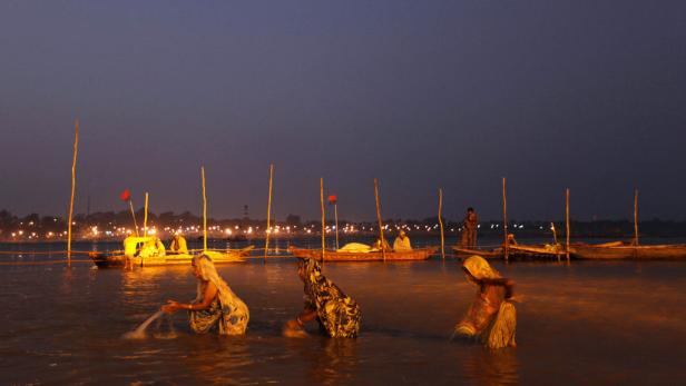Frauen waschen sich im Ganges bei Dämmerung, während Boote auf dem Fluss treiben.